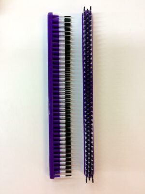 A purple and black plastic comb on top of a white wall.