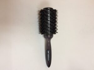 A black round brush with long handle on top of white surface.