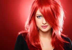 Woman with striking red hair and captivating blue eyes against a red background.